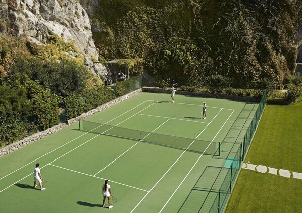 A tennis court with a net, surrounded by greenery and a stone wall. - Il San Pietro di Positano (Positano)