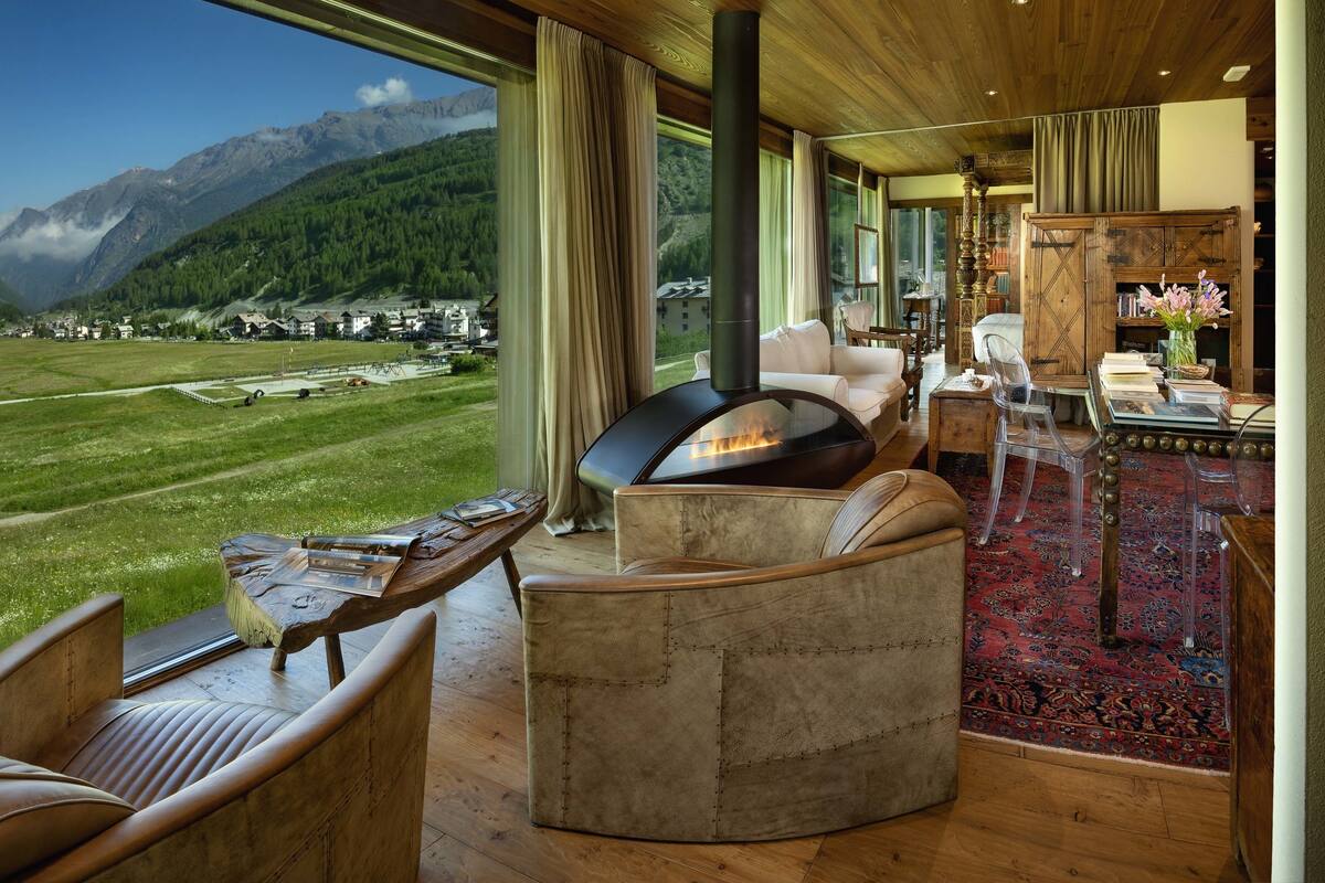 A cozy living room with a fireplace, comfortable seating, and a large window overlooking a mountainous landscape.