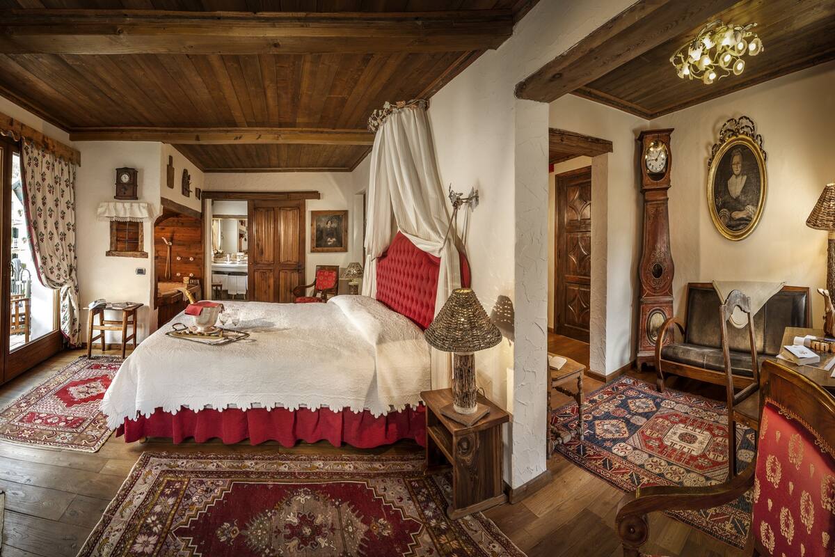 A traditional room with a bed, a fireplace, a wooden ceiling, and a large window.