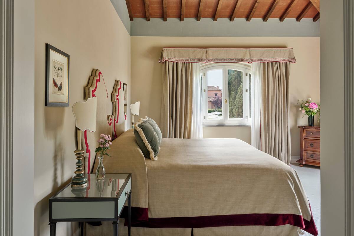 Une chambre à coucher comprenant un lit, une table de chevet, une fenêtre avec des rideaux, une commode et un tableau encadré accroché au mur.