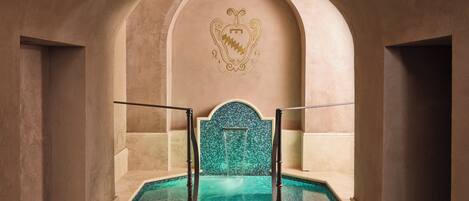 An arched entrance leading to a pool area with a decorative emblem on the wall.