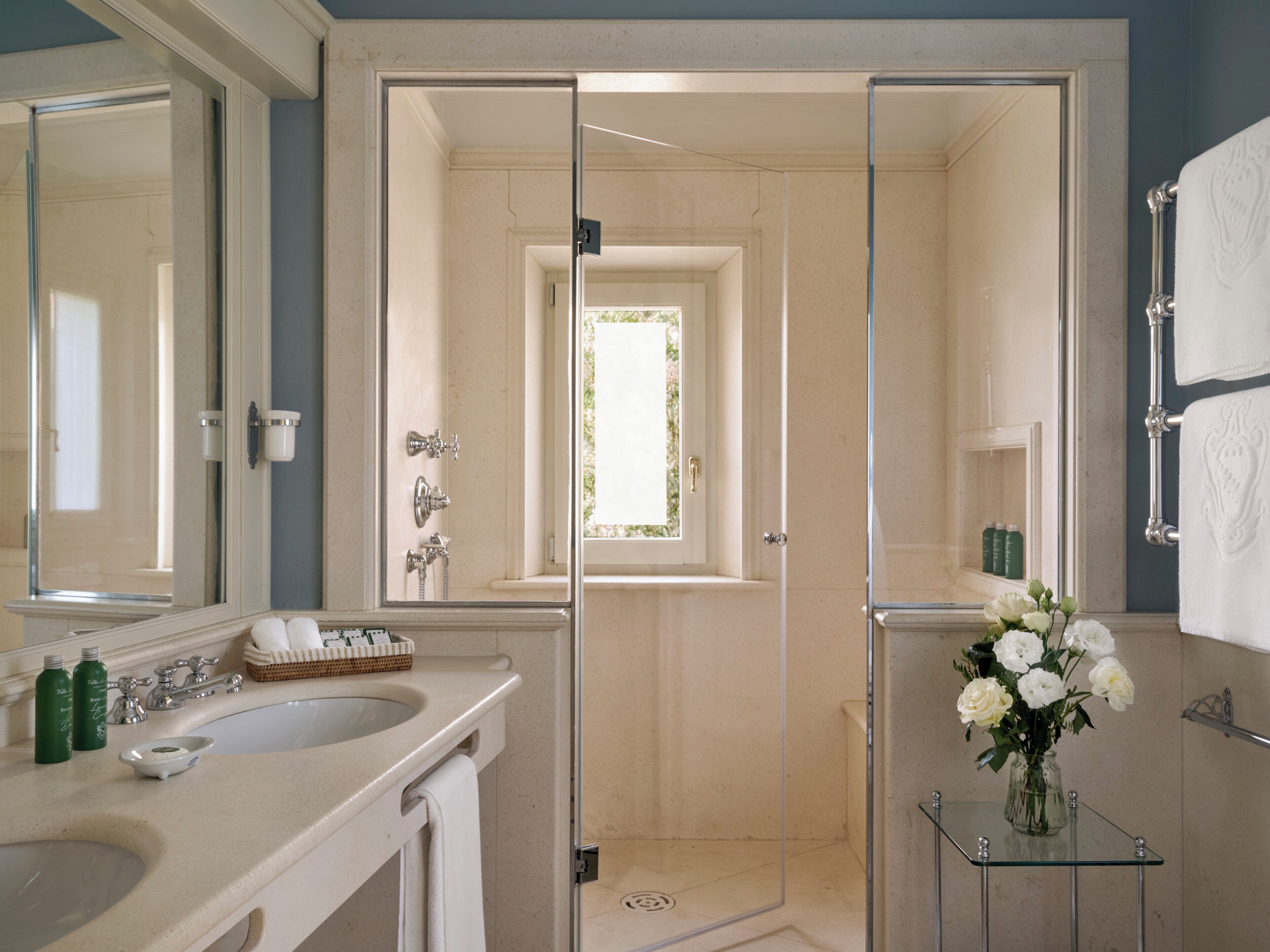 Une salle de bain moderne dotée d’une douche à parois de verre, d’un grand miroir et d’un meuble-lavabo avec un évier et des articles de toilette.