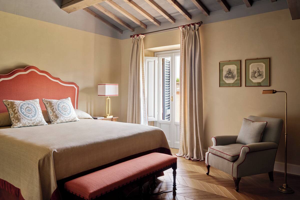 Une chambre à coucher comprenant un lit, un banc, une chaise, une table de chevet, une lampe et des rideaux.