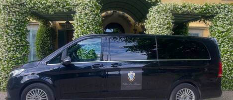 Un fourgon noir est garé devant un immeuble orné d’un auvent vert et de fleurs blanches.