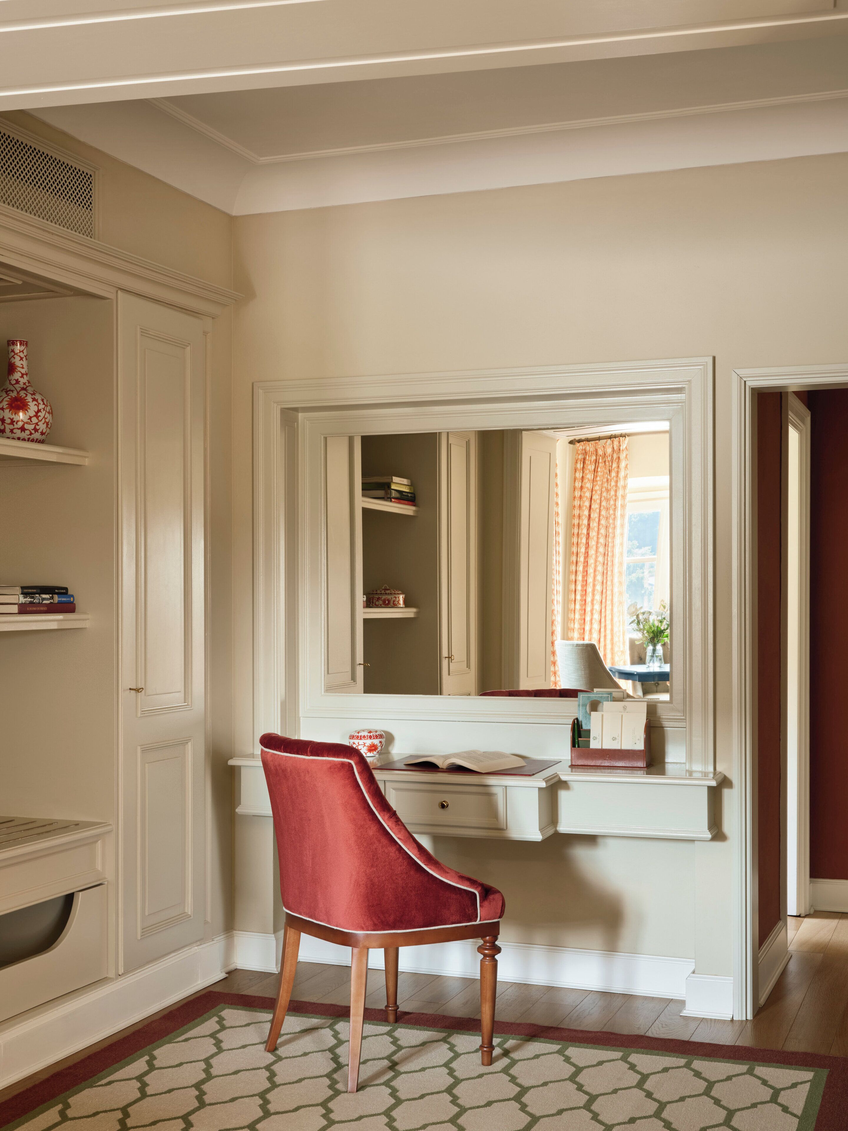 A room with a red chair, a white vanity with a mirror, and a bookshelf.