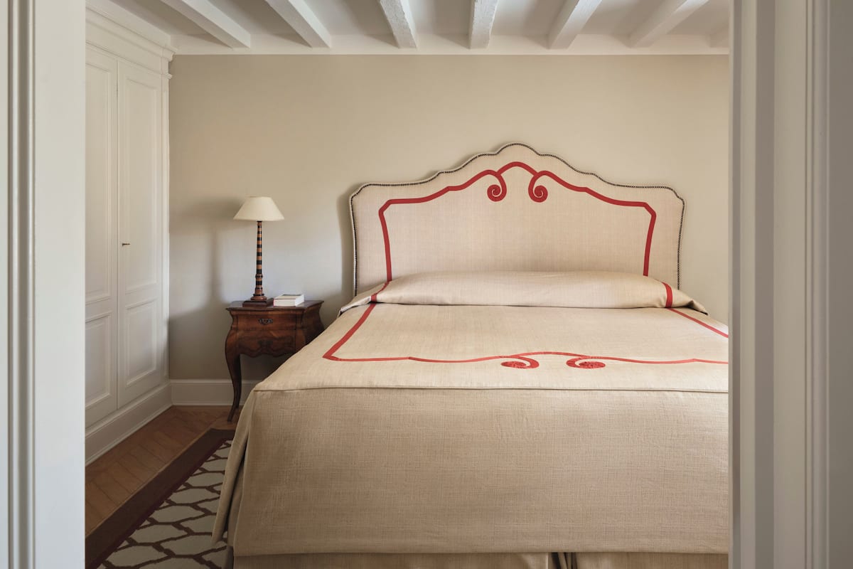 Un lit bien fait, avec une tête de lit, une table de chevet avec une lampe et un tapis à motifs sur un plancher en bois.