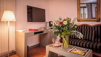 A modern living room with a flat-screen TV, a sofa, a coffee table with a vase of flowers, and a lamp.