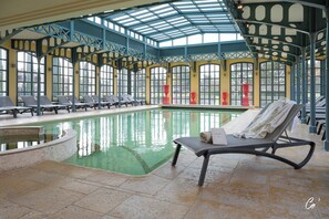An indoor swimming pool with lounge chairs and a covered roof structure.