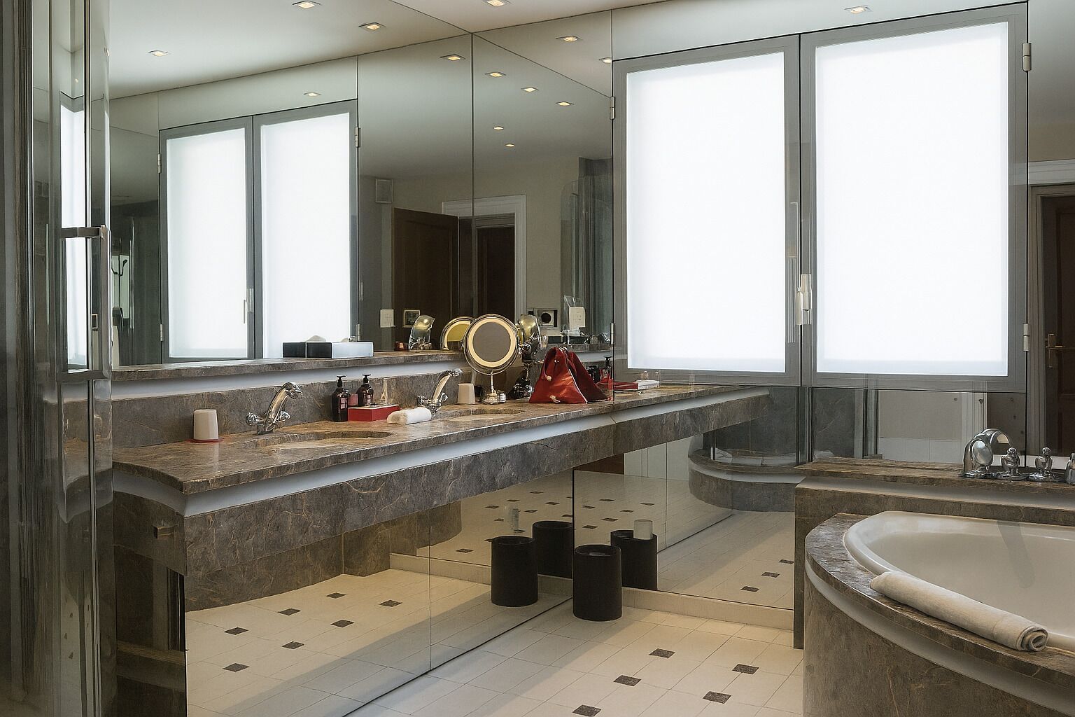 A modern bathroom with dual sinks, a large mirror, and a bathtub.