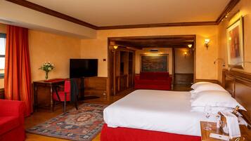 A hotel room with a large bed, a desk with a chair, a television, a red sofa, and a painting on the wall.