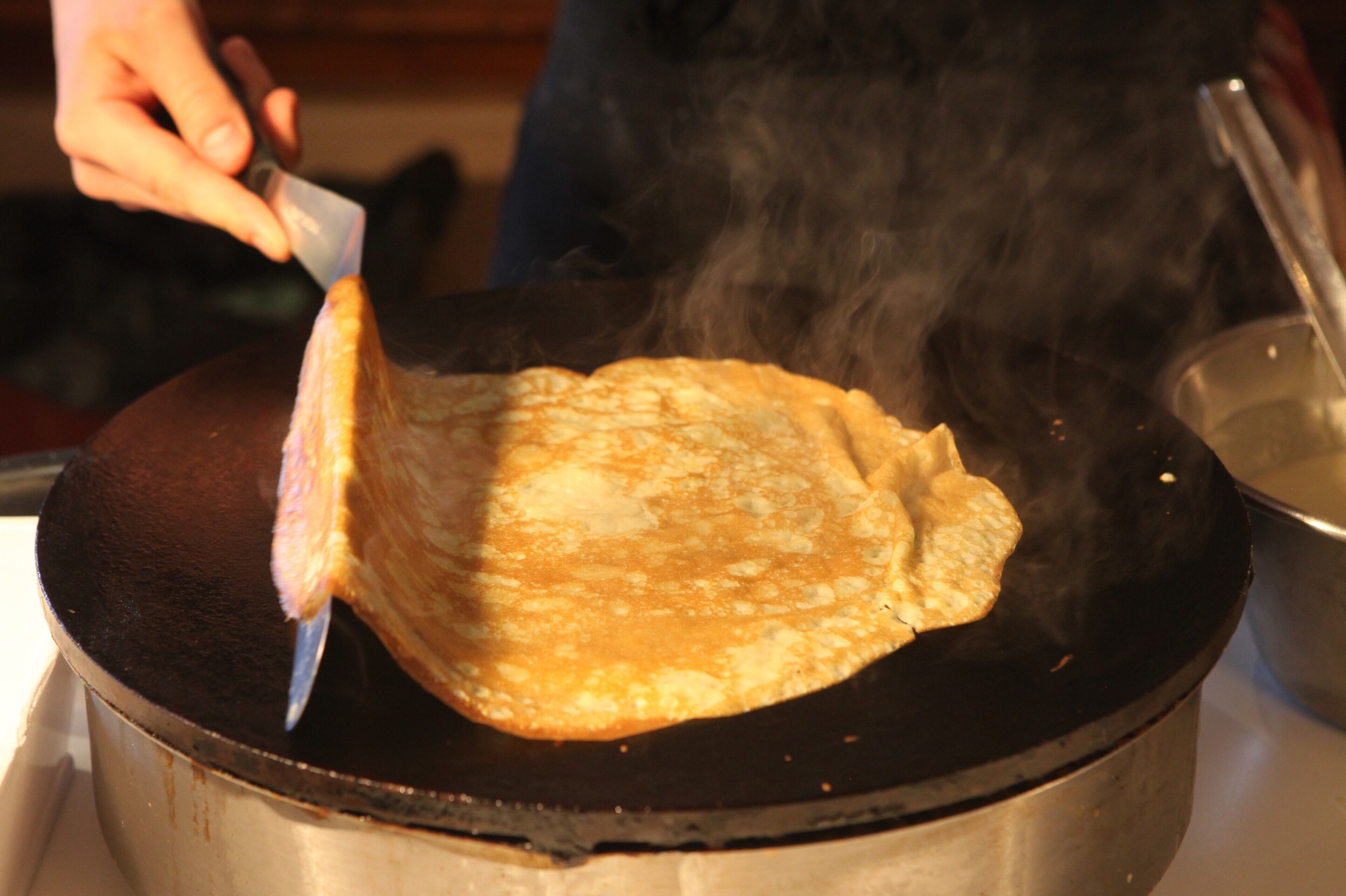Una persona cocinando un pan plano sobre una superficie caliente, con vapor ascendiendo.