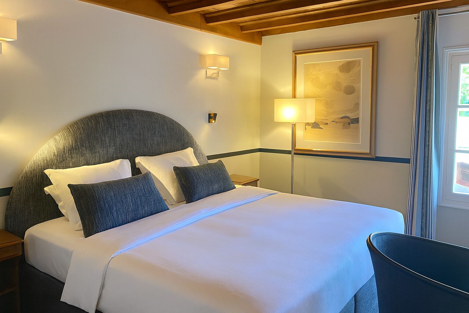 Habitació d'hotel amb un llit gran, un capçal de llit, taules de nit, una làmpada i un quadre amb marc a la paret.