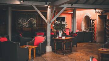 A cozy interior with wooden beams, red upholstered chairs, and a tiled floor.