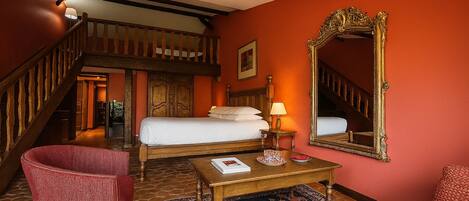 Habitación de hotel con cama, un espejo grande, un escritorio de madera, una silla roja y una escalera.