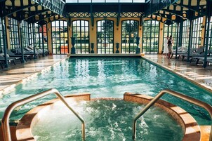 Una piscina interior con agua cristalina, rodeada de sillones de descanso y una zona cubierta con ventanas amplias.
