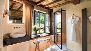 Un baño con un lavamanos grande, un banco, un espejo y una ventana con cortinas.