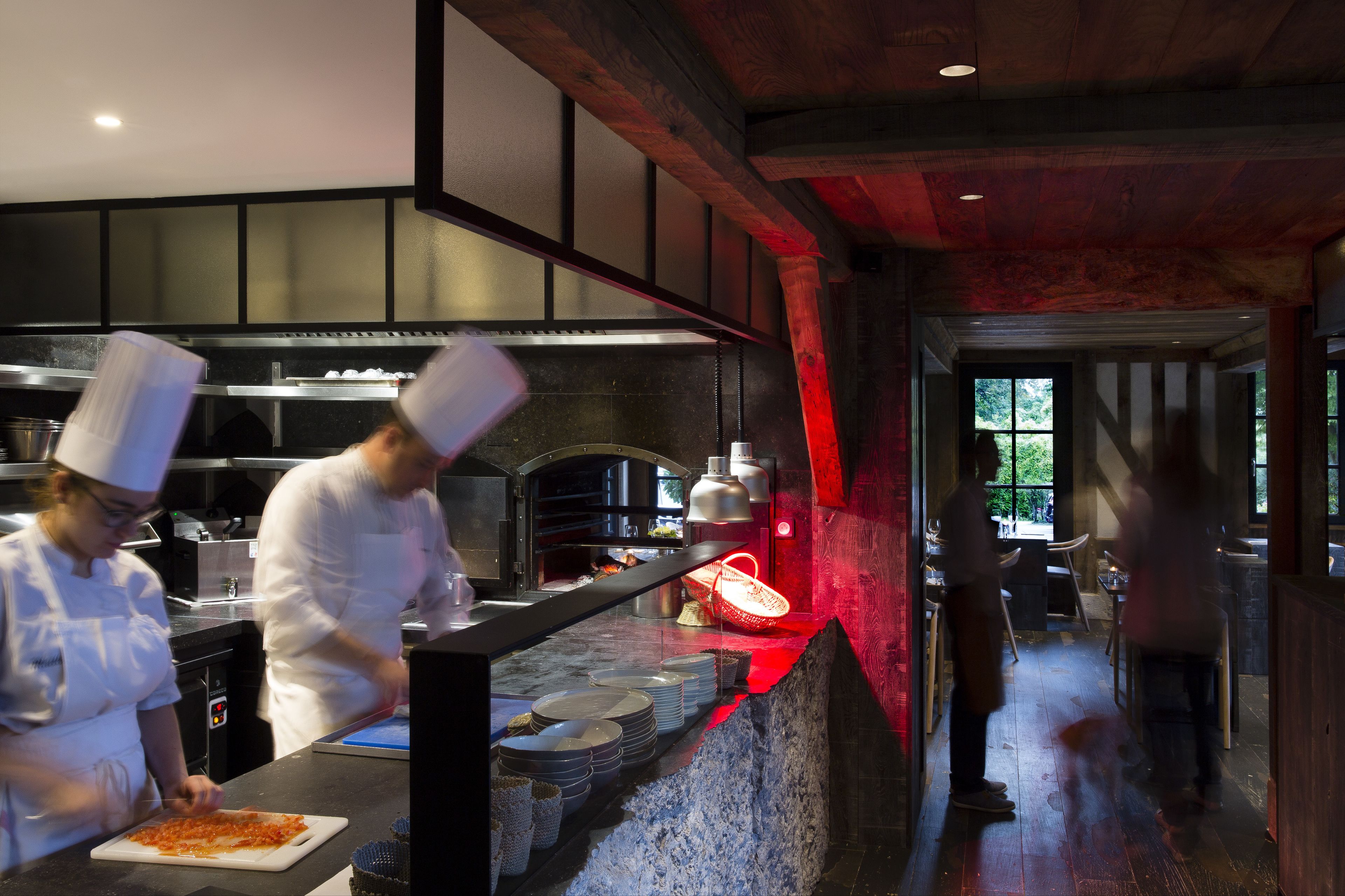 A professional kitchen with chefs preparing food, a pizza station, and a wood-paneled interior.