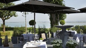 Un espace extérieur aménagé pour les repas, avec des tables, des chaises, des parasols et une vue sur l’eau.