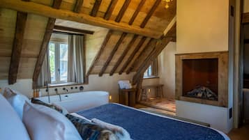 Ein Schlafzimmer mit Holzboden, einem großen Bett, einem Kamin und einem Fenster.