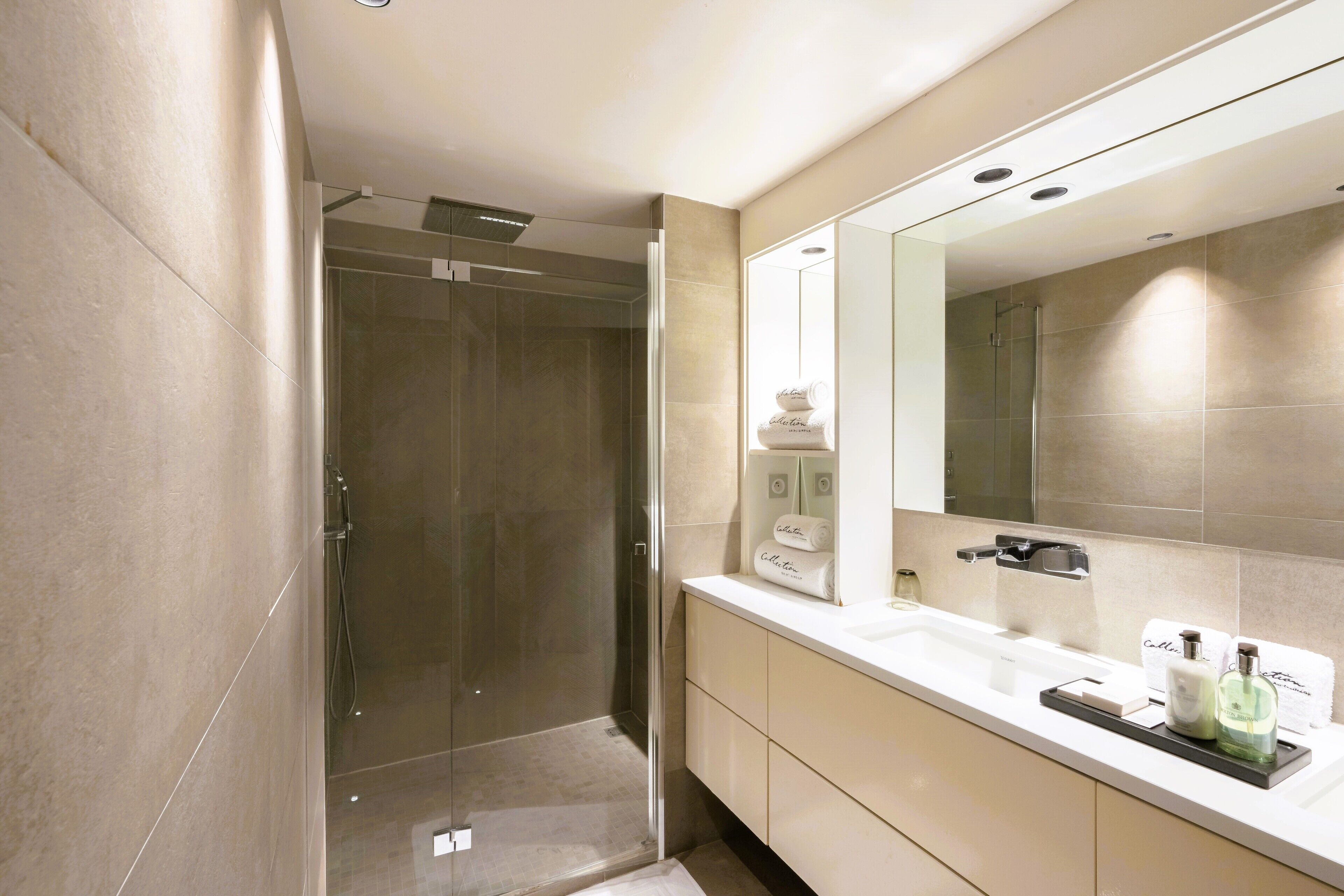 Een moderne badkamer met een douchecabine van glas, een grote spiegel en een witte wastafel met toiletartikelen.