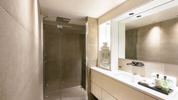 Een moderne badkamer met een douchecabine van glas, een grote spiegel en een witte wastafel met toiletartikelen.