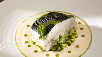 A white plate with a piece of white fish, green peas, and a green sauce.