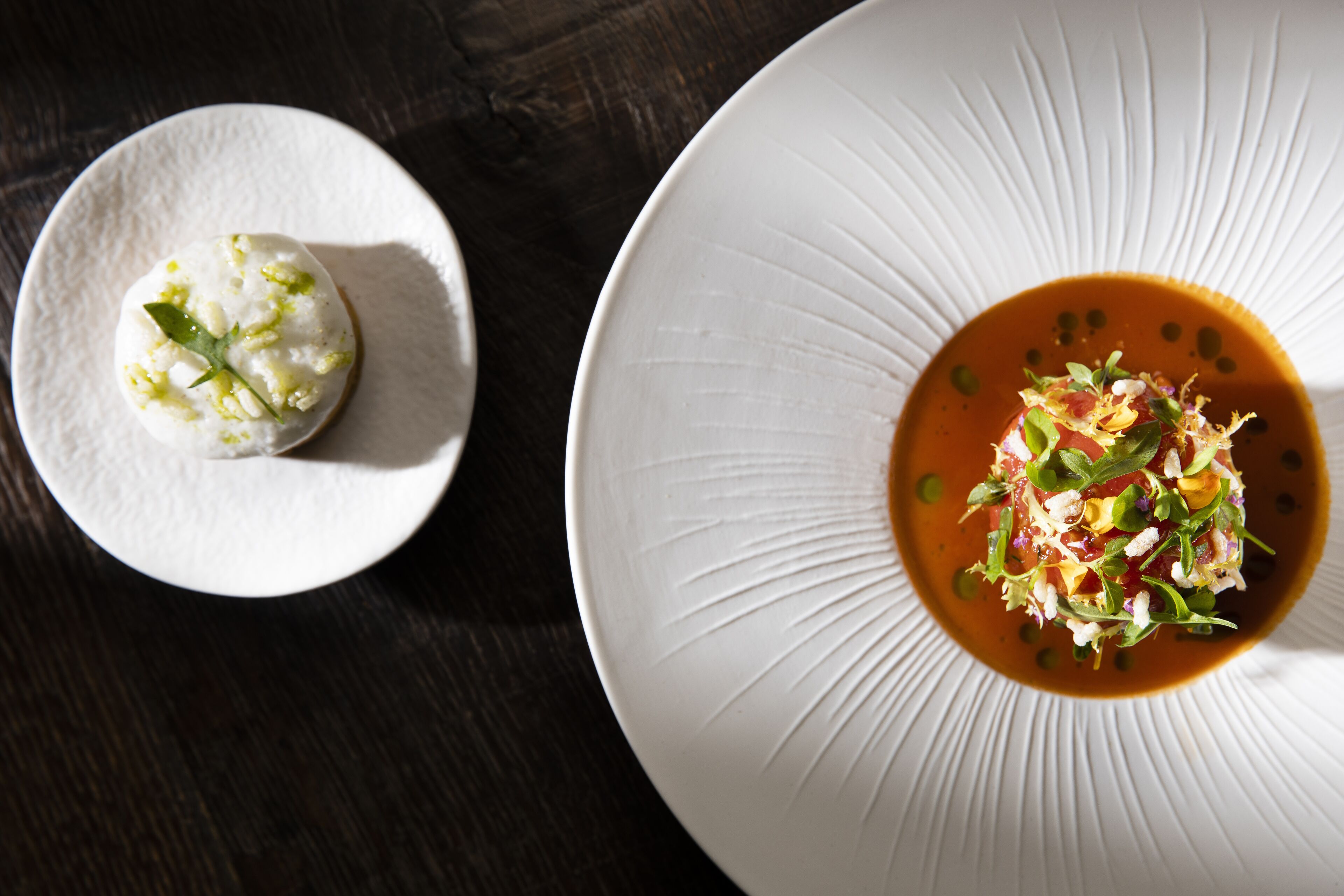 Two plates of food, one with a white sauce and the other with a red sauce, on a dark wooden table.