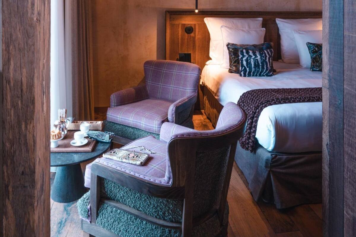 A cozy room with a bed, a chair, a small table with a tray of items, and a hanging light fixture.