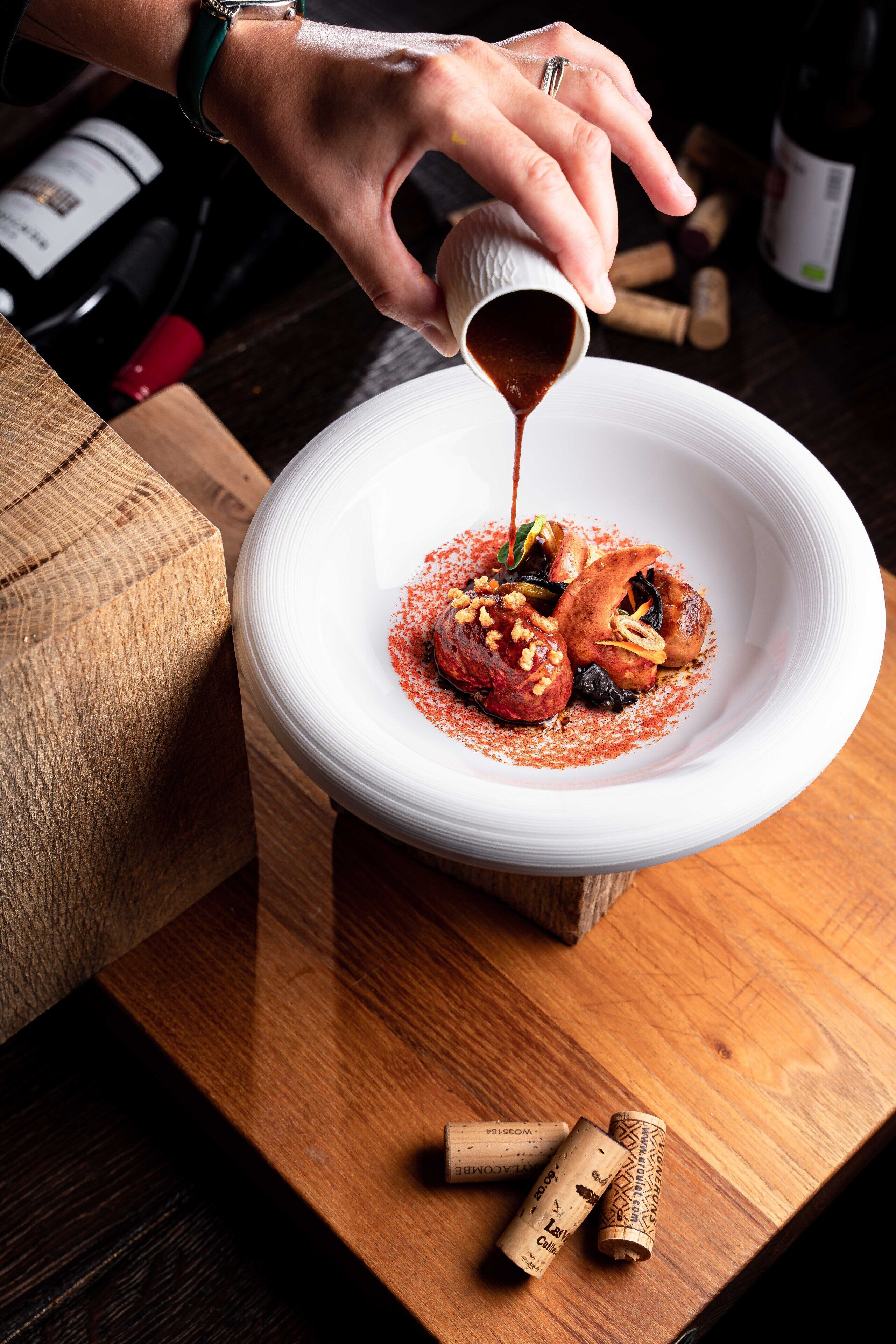 Une personne verse de la sauce sur un plat contenant des aliments, et des bouchons de liège sont posés sur une table en bois.