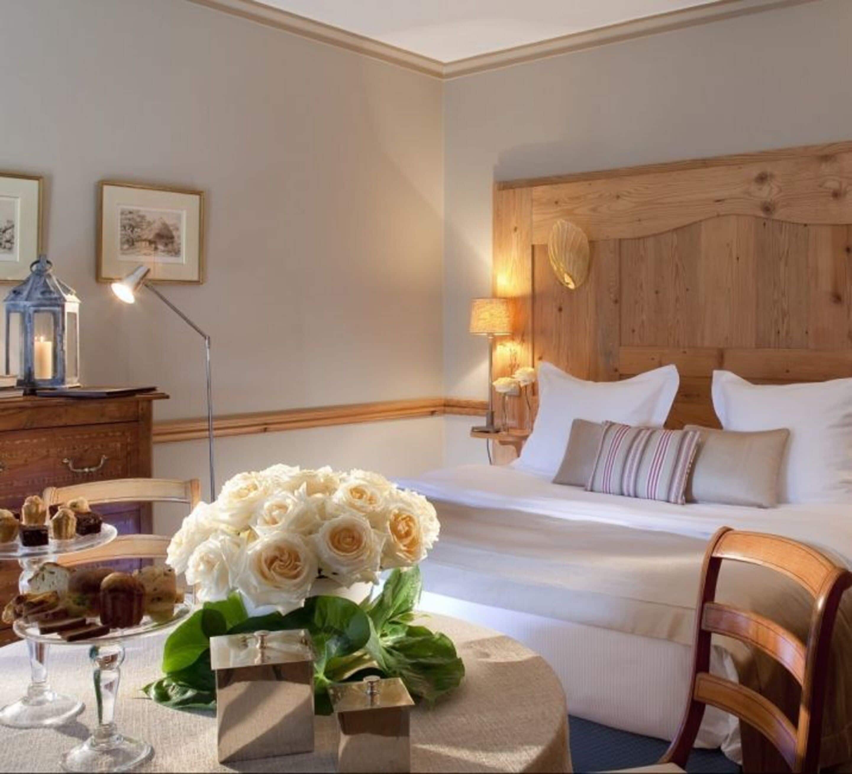 Une chambre d’hôtel comprenant un lit, des lampes de chevet, un bureau avec une lampe, une table agrémentée d’un bouquet de fleurs et une chaise.