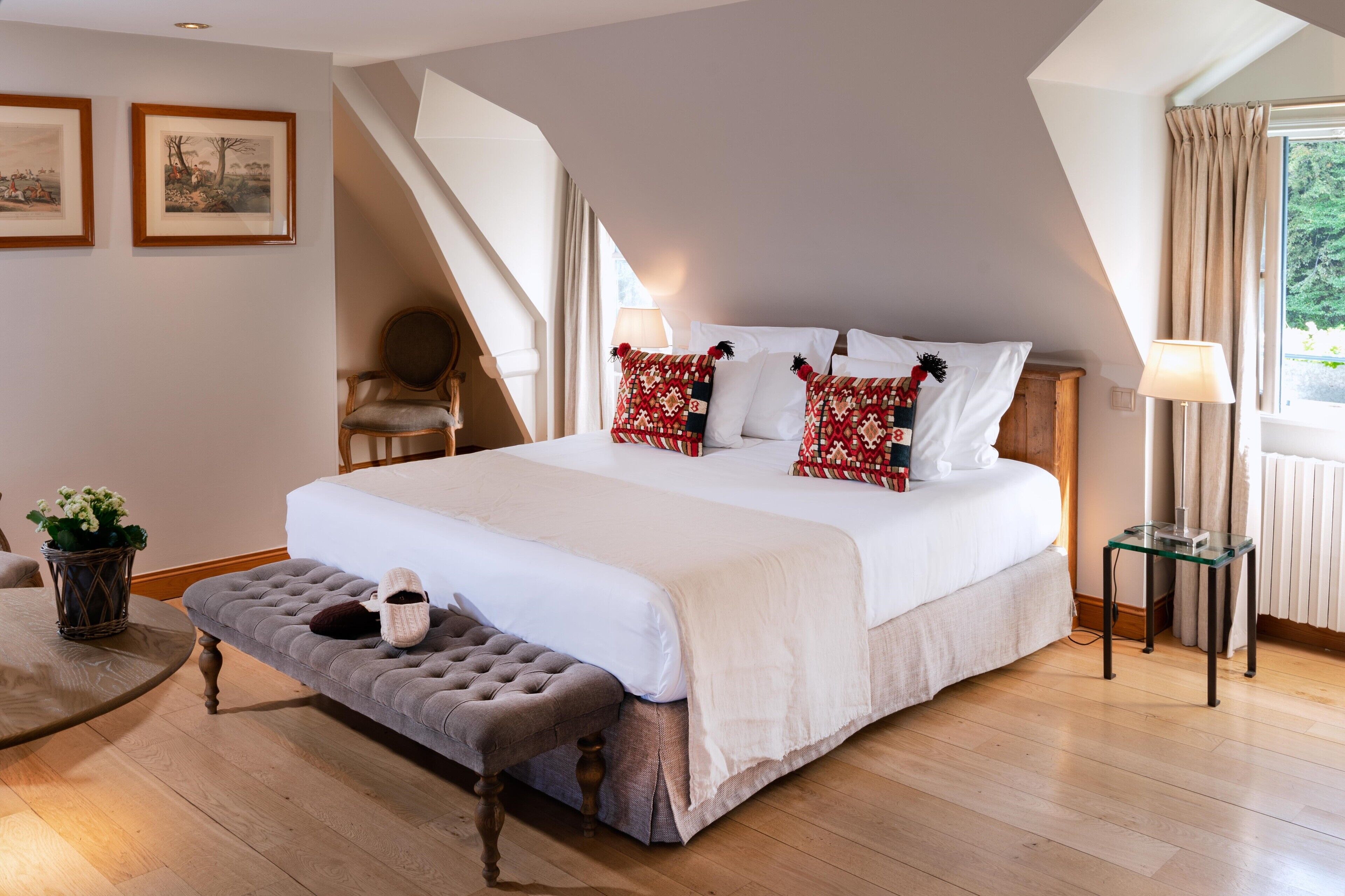 A bedroom with a large bed, a bench, a chair, a table, and a window with curtains.