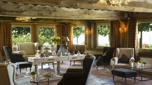 Un vaste salon doté d’un plafond en bois, de grandes fenêtres avec des rideaux et de plusieurs coins salon.