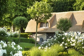 A traditional thatched-roof house surrounded by well-maintained gardens and white flowering plants. - La Ferme Saint Simeon (Honfleur)