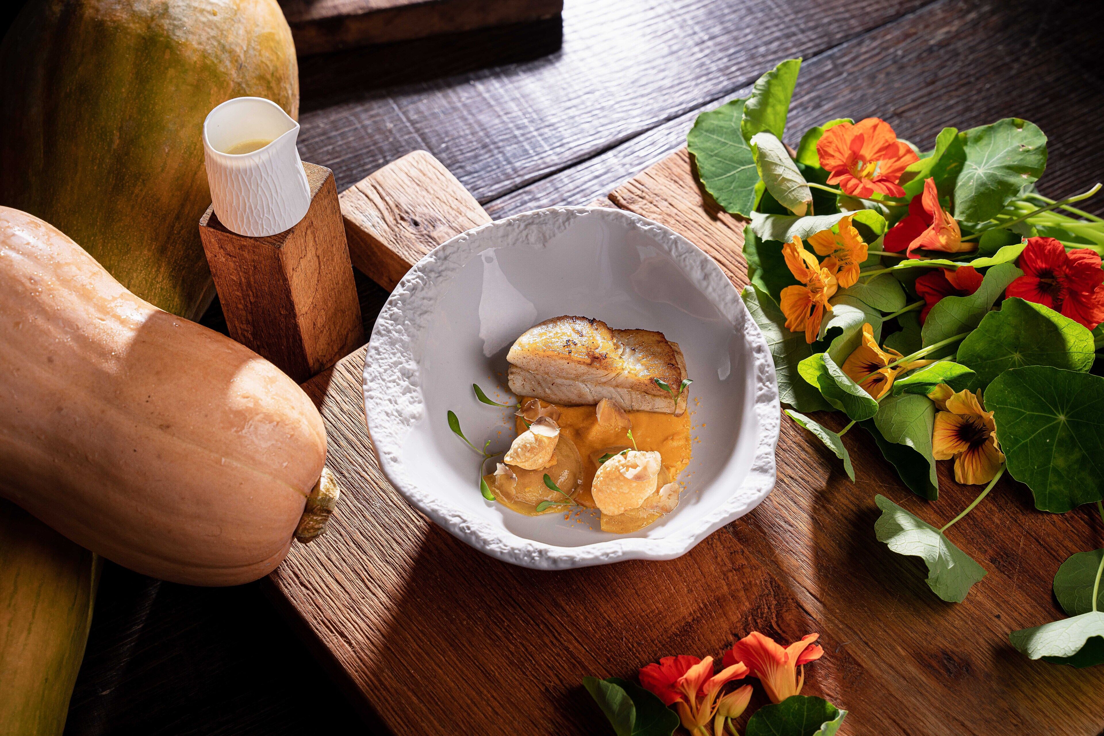 Une table en bois sur laquelle se trouve un bol blanc contenant un plat, une carafe en bois et une courge.