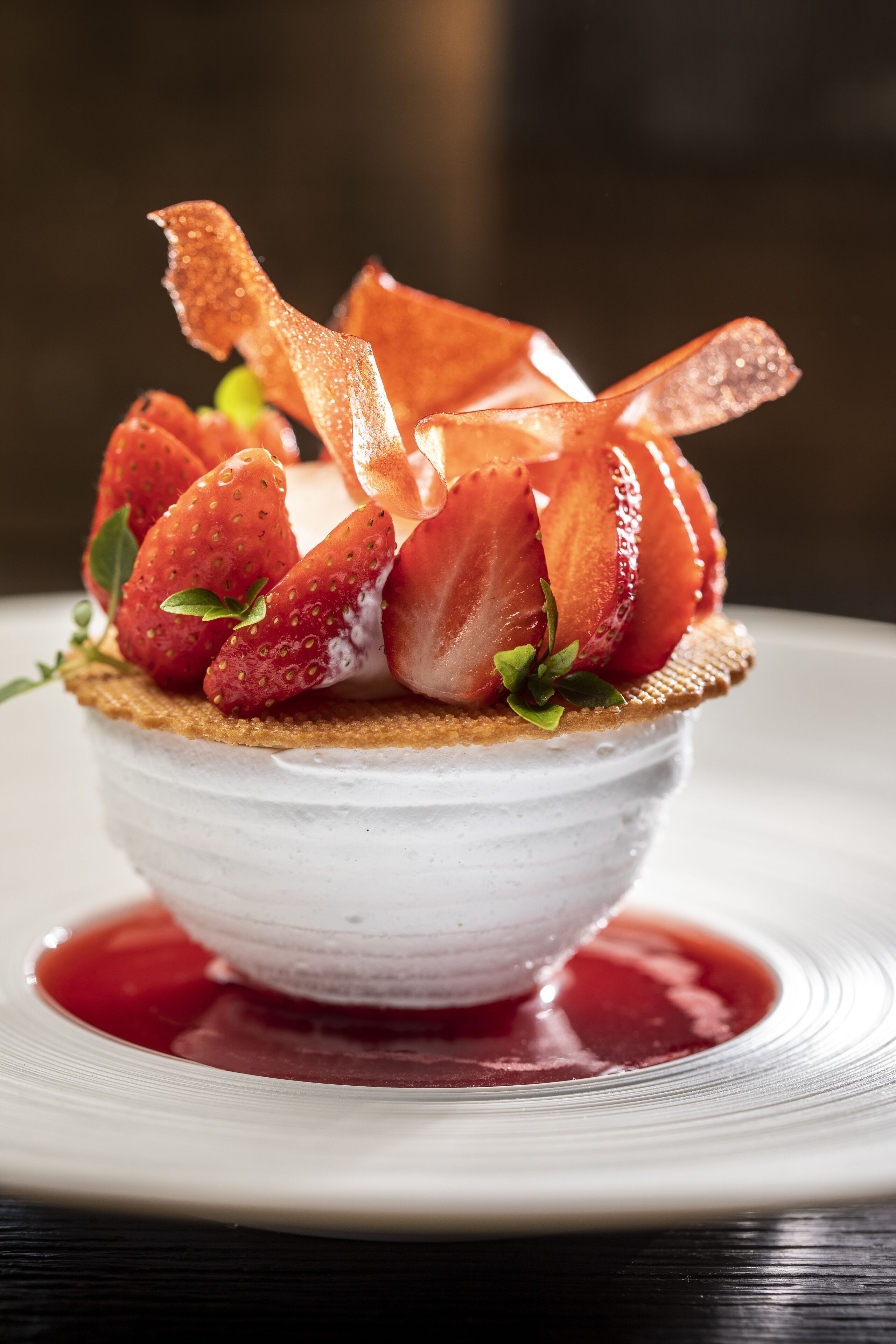 A dessert with strawberries and a crispy element on top, served on a white plate with a red sauce.