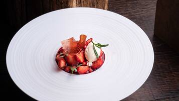 A white plate with a dessert consisting of strawberries, a scoop of ice cream, and a garnish of herbs.