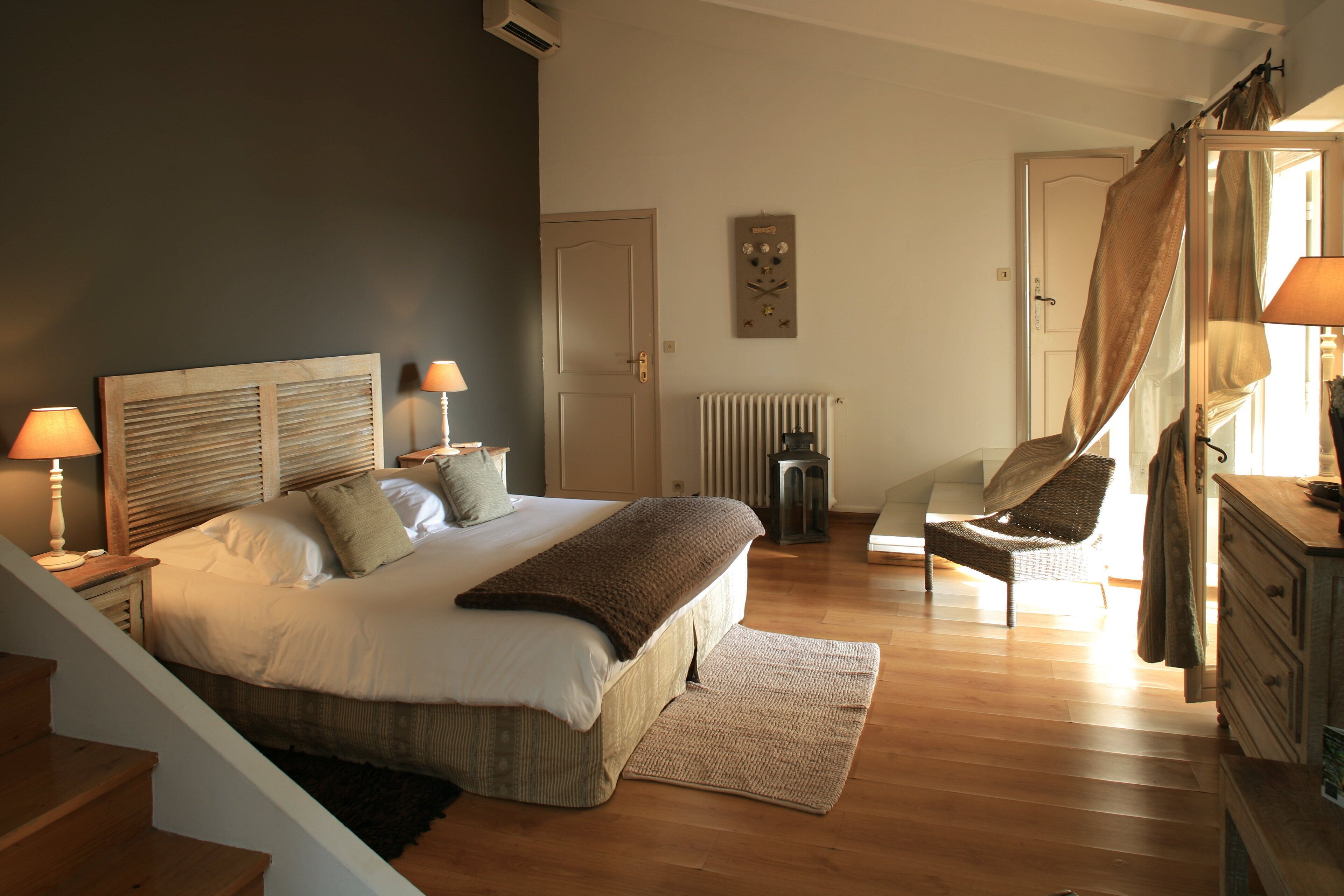 A bedroom with a bed, bedside lamps, a chair, a dresser, and a radiator.
