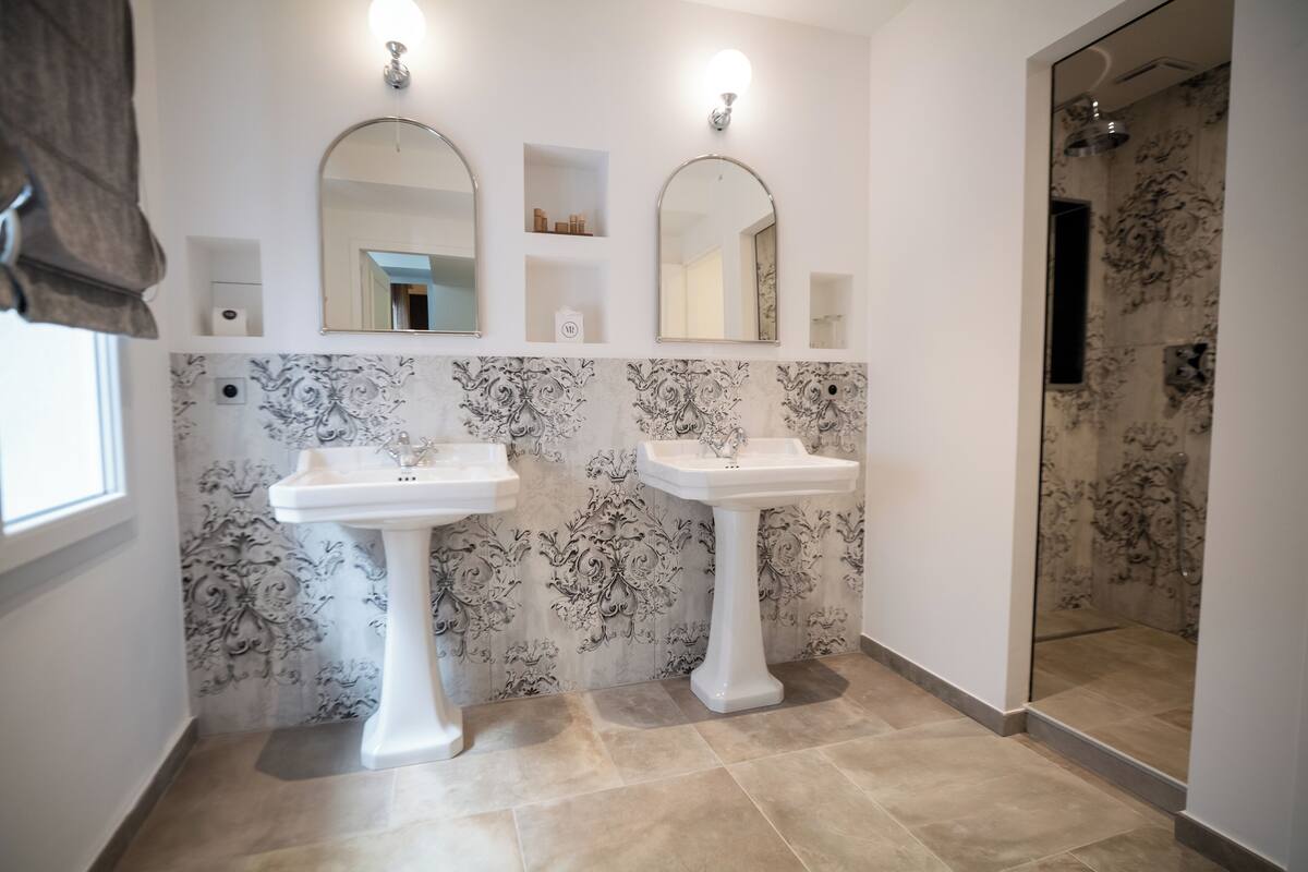 A bathroom with two pedestal sinks, a large mirror above each, and a shower area with a glass door.