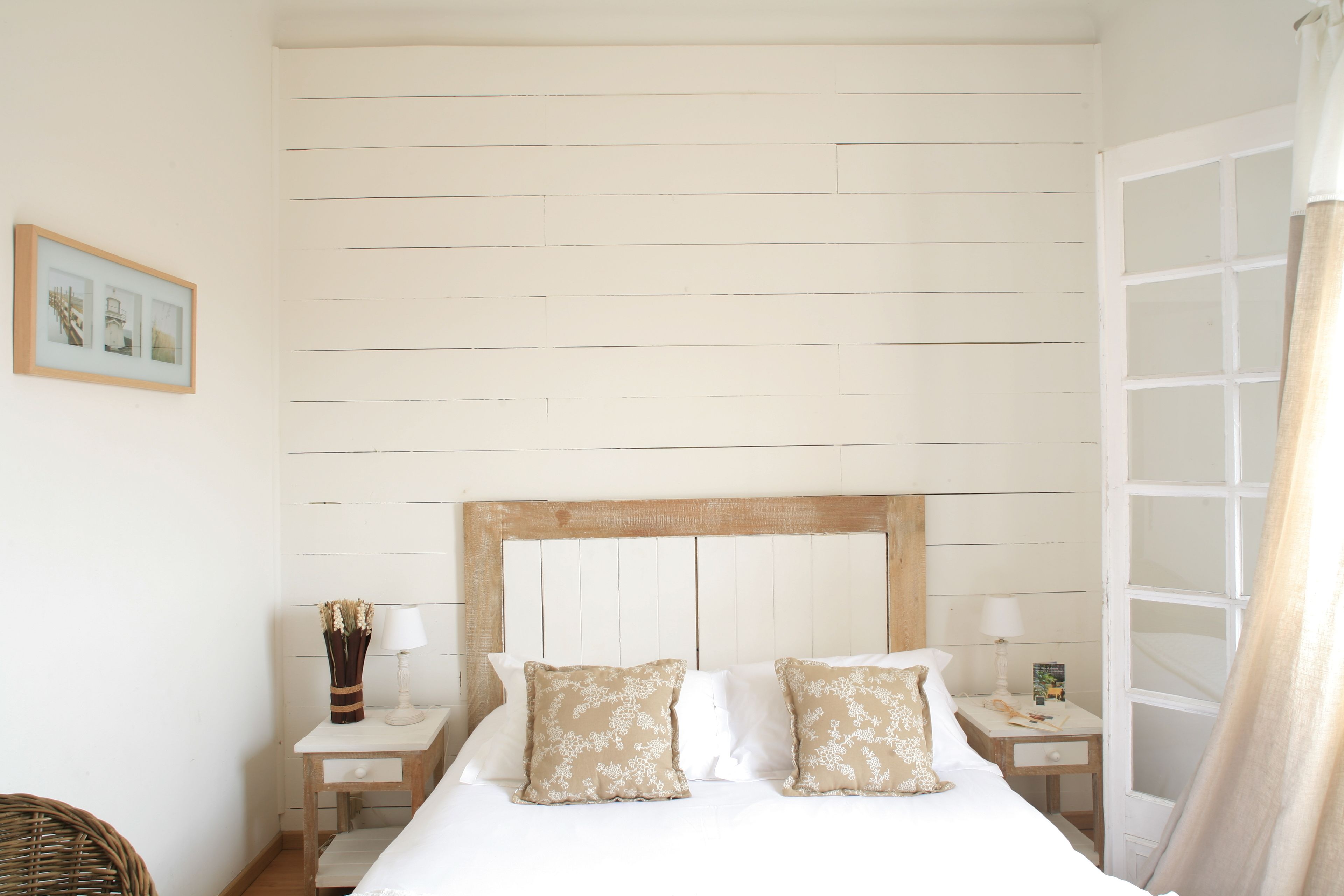 Un dormitorio ordenado con una cabecera de madera, dos mesitas de noche con lámparas y un cuadro en la pared.