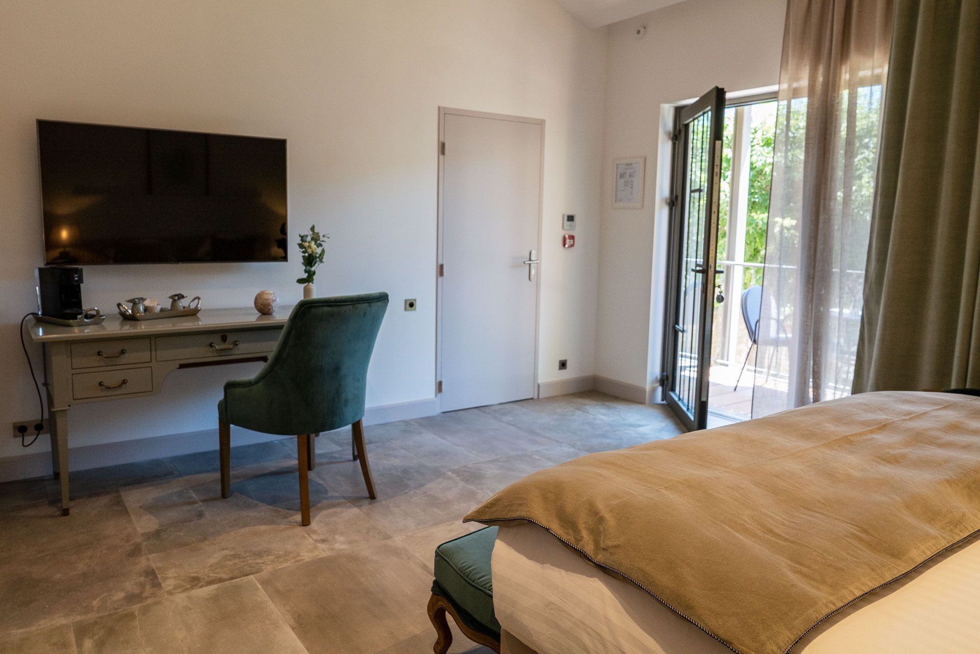 Un dormitorio con cama, escritorio, silla, televisor y puerta corrediza de vidrio a un balcón.