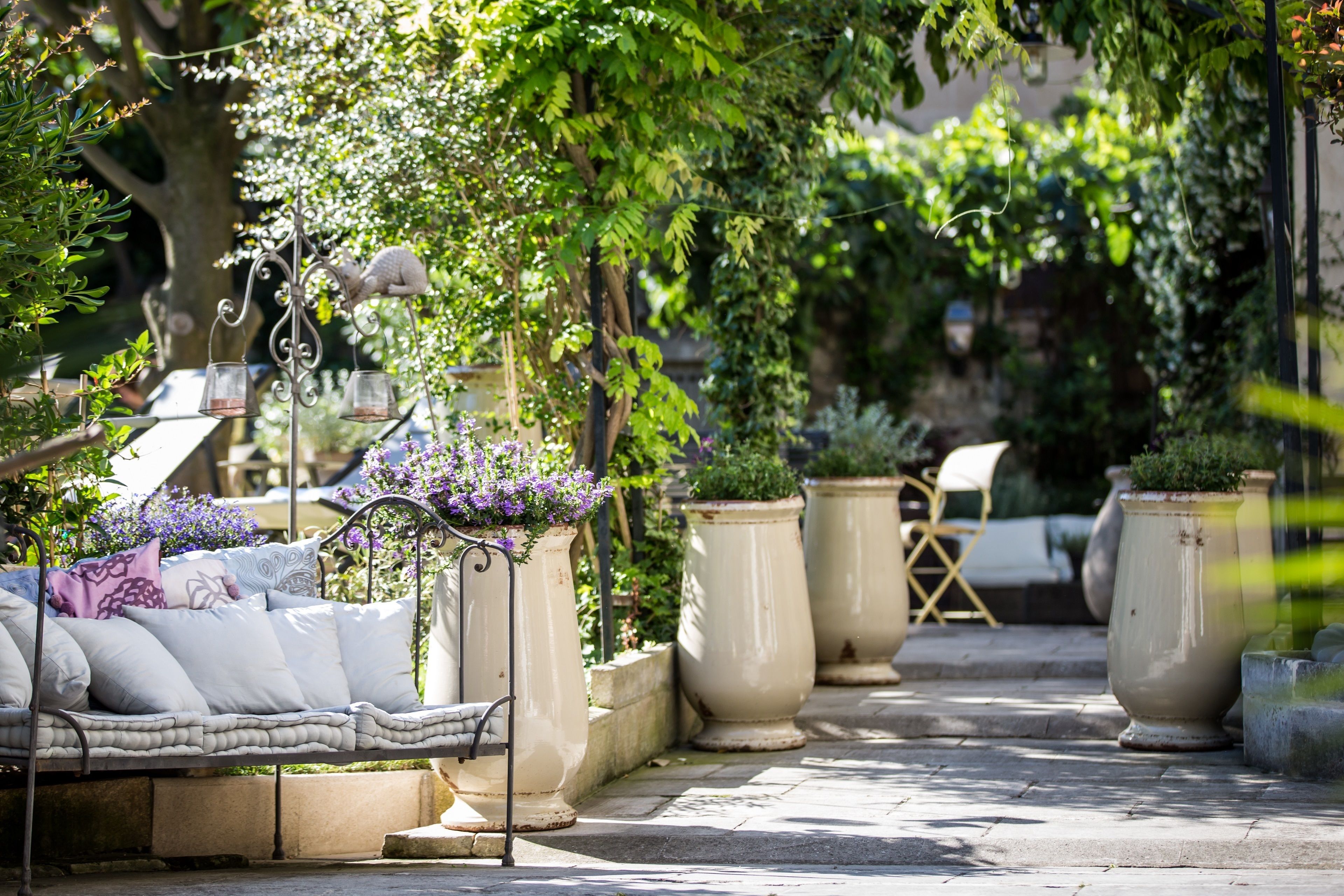 A garden patio with a cushioned seating area, large planters, and hanging candle lanterns.