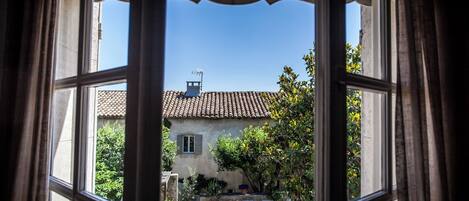 A view through a window of a building with a tiled roof, a swimming pool, and outdoor seating.