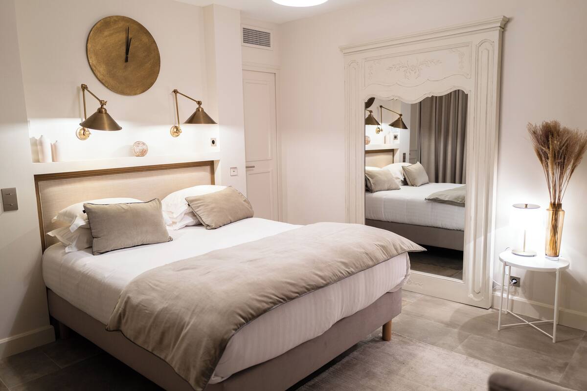 A neatly arranged bedroom with a large bed, bedside lamps, a mirror, and a small table with a vase.