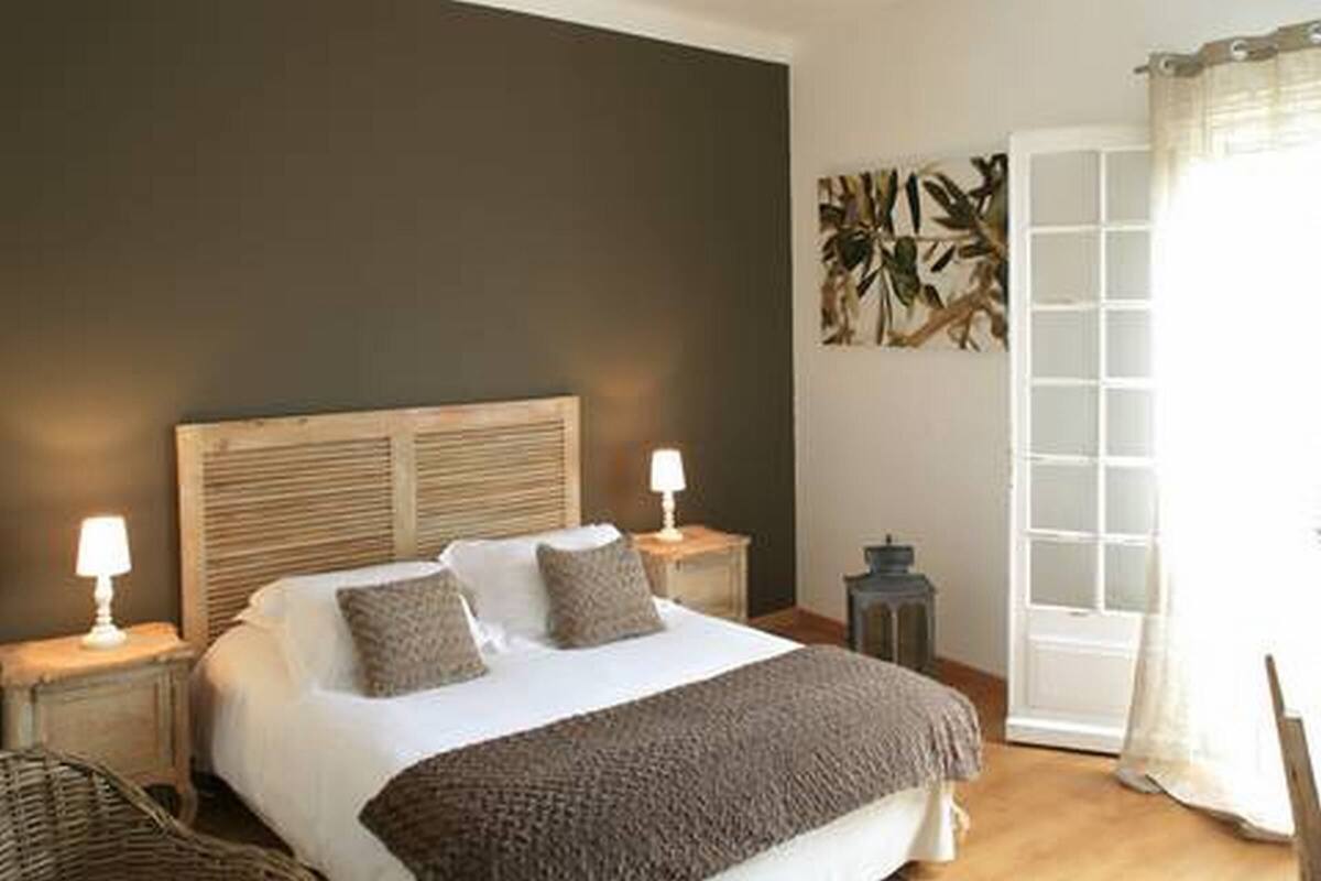 A bedroom with a bed, two bedside tables, a lamp, a door, and a wall art piece.