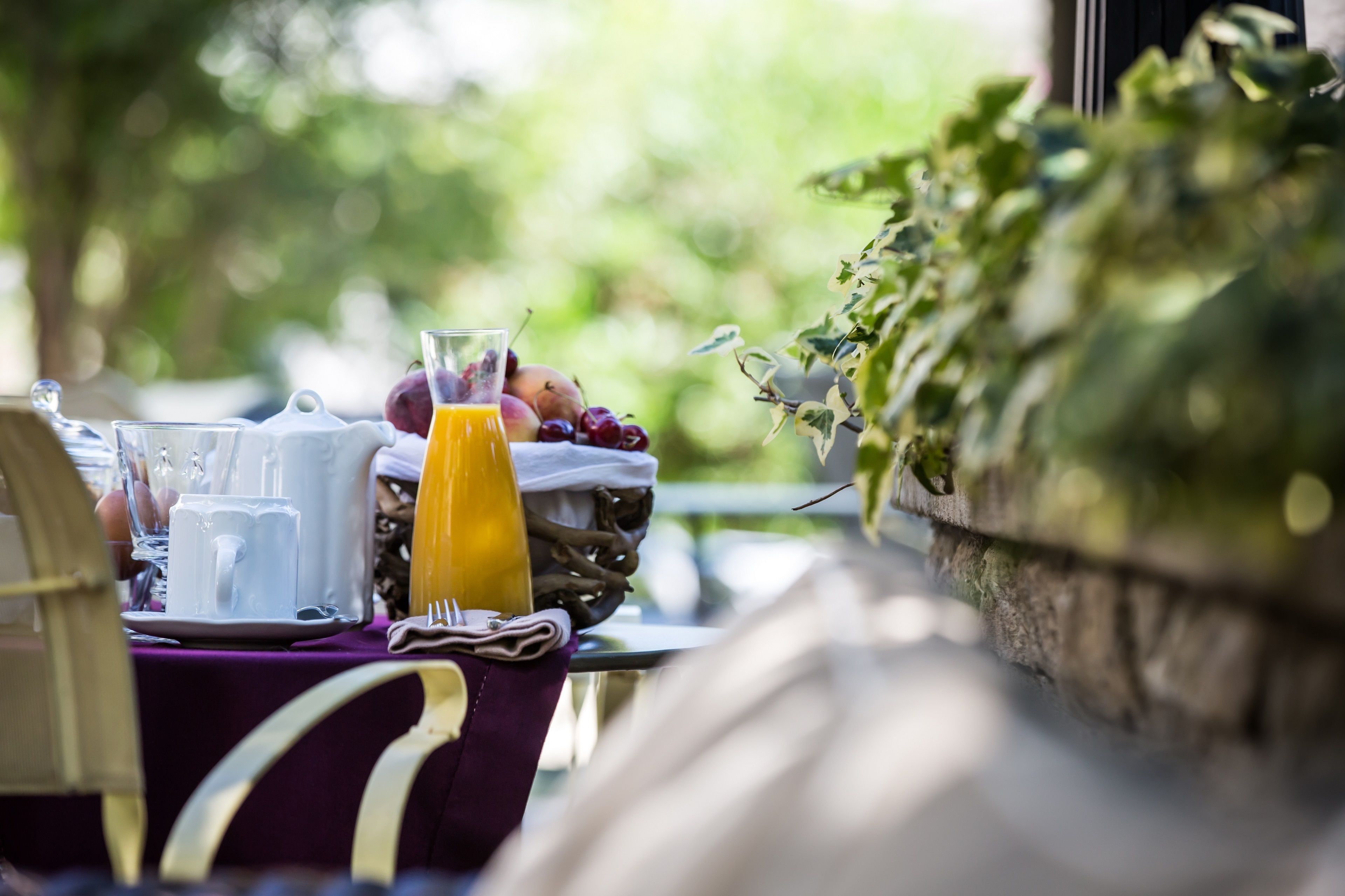 A breakfast table with a pitcher, cups, a glass of orange juice, and fresh fruit.