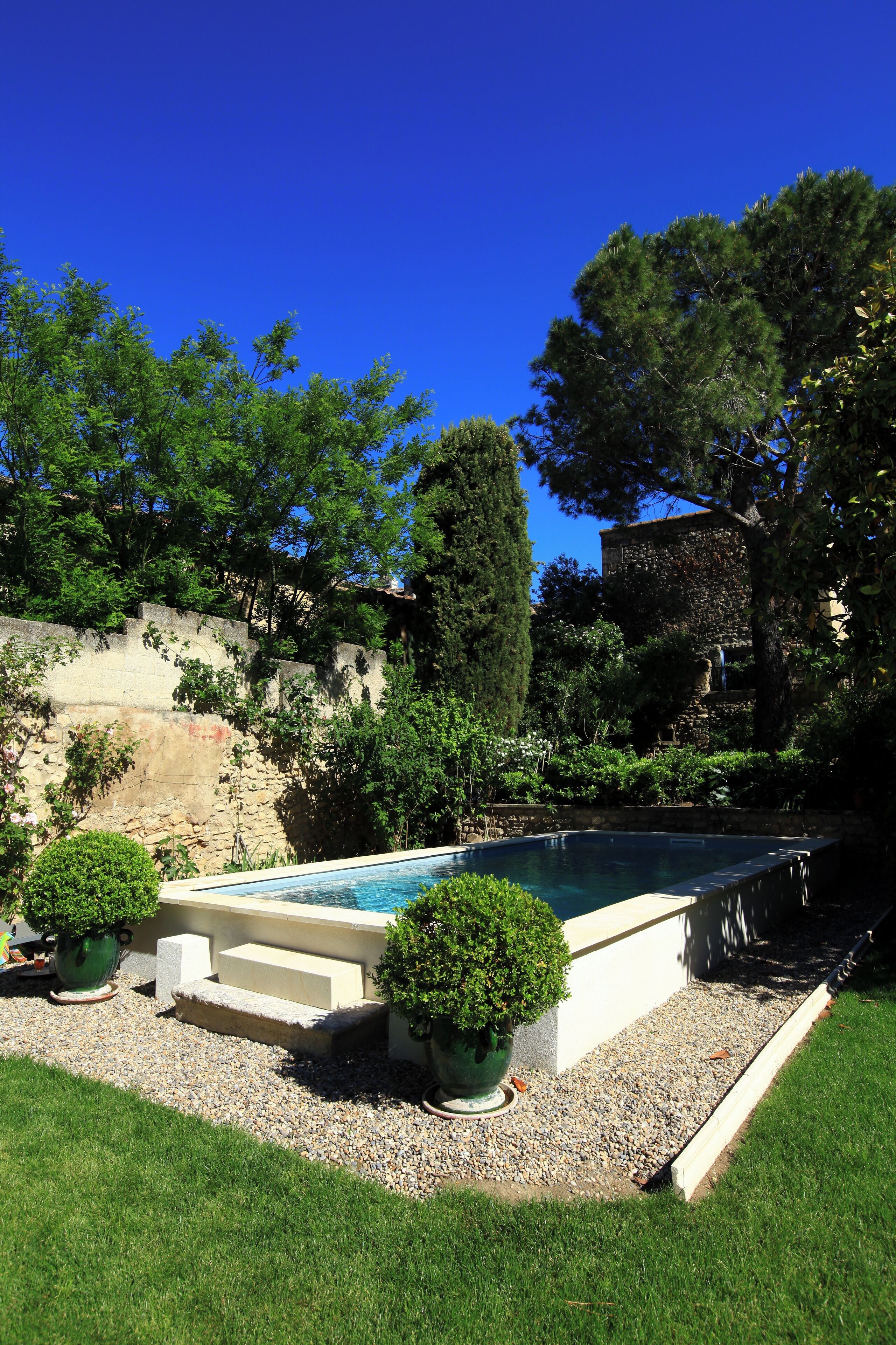 A swimming pool surrounded by a well-maintained garden with a stone wall and a large tree.
