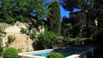 A swimming pool surrounded by a well-maintained garden with a stone wall and a large tree.