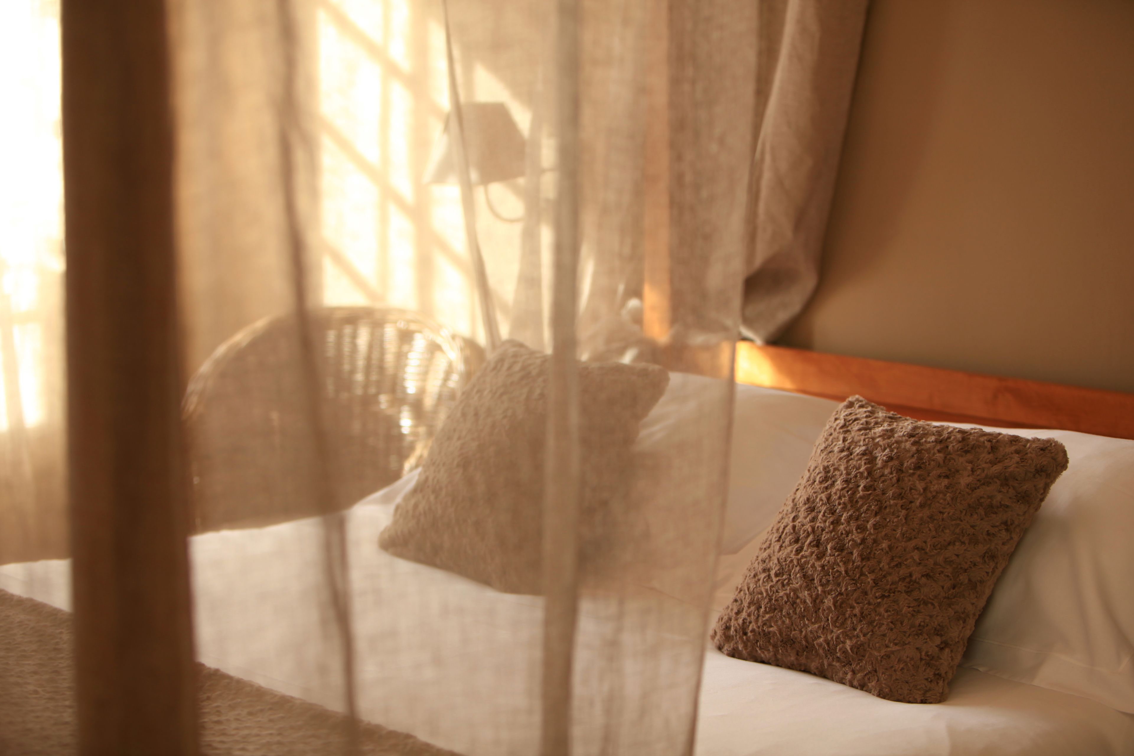 A room with a bed, a window with sheer curtains, and a wooden headboard.