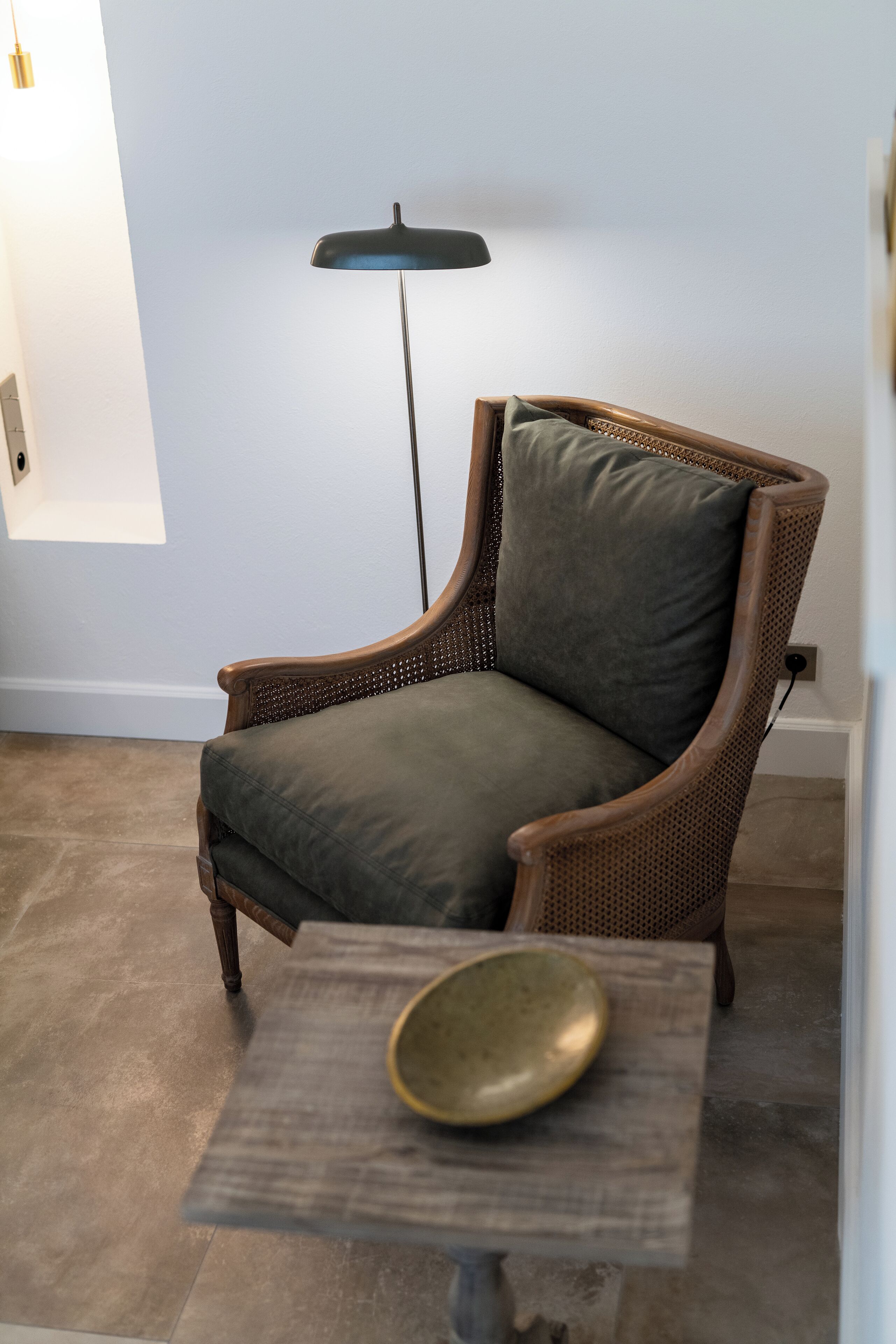 A wicker armchair with a cushion, a floor lamp, and a small table with a bowl.