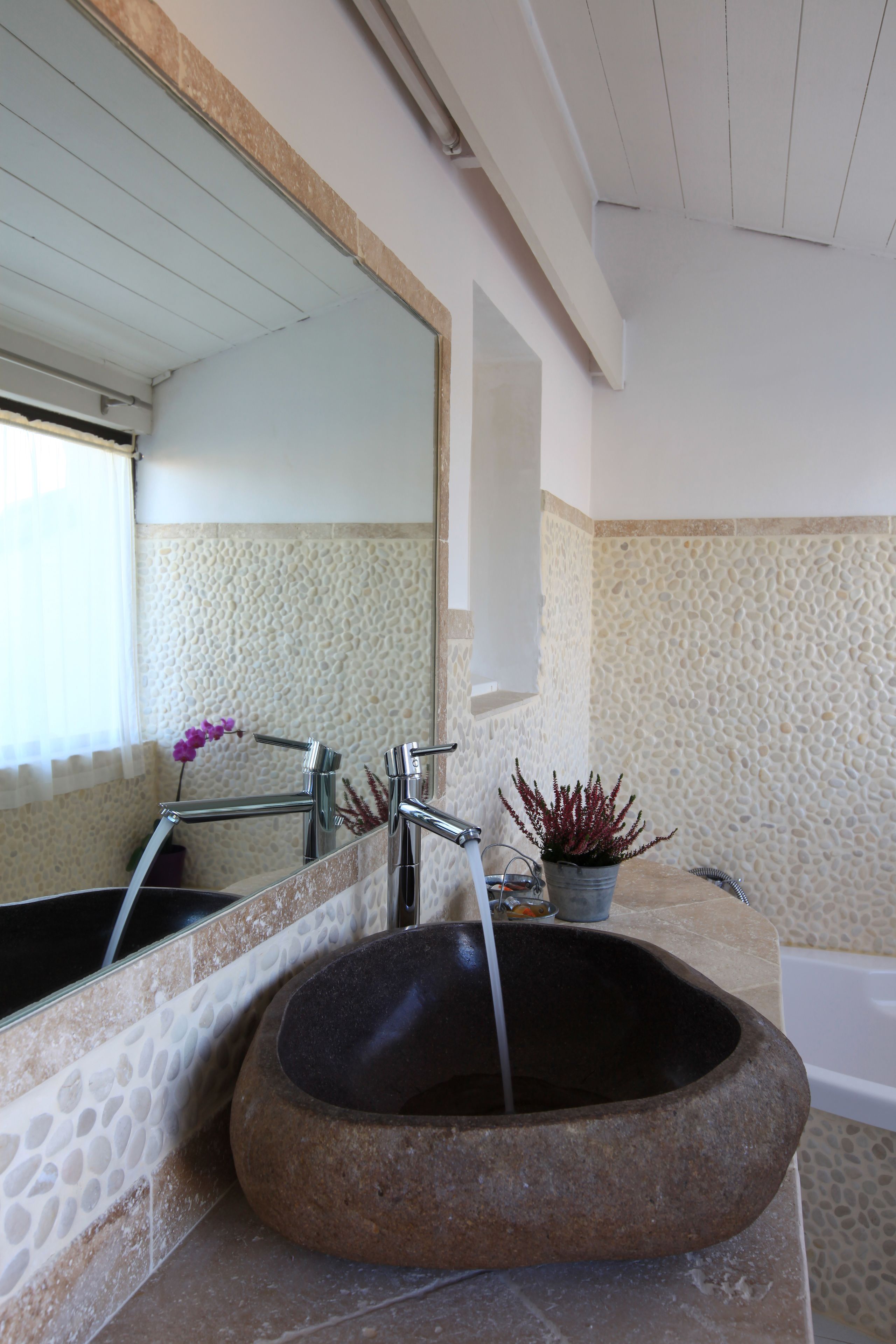 A bathroom with a stone sink, a mirror, and a bathtub.